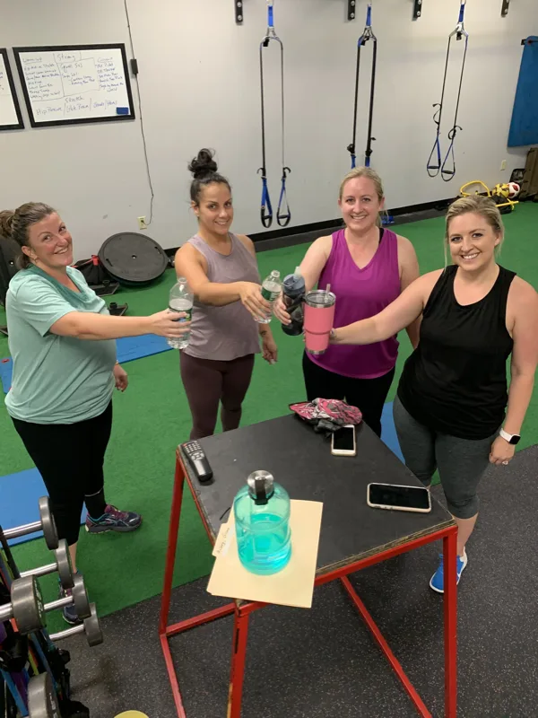 Two members smiling while holding kettlebells